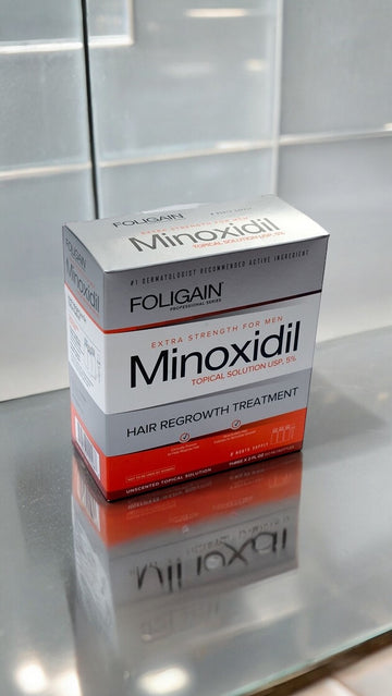 علبة محلول مينوكسيديل FOLIGAIN الموضعي بتركيز 5% على سطح عاكس.