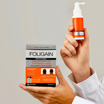يدان تحملان علبة وزجاجة رش علاج FOLIGAIN الموضعي للرجال بتركيز 10% من TRIOXIDIL.