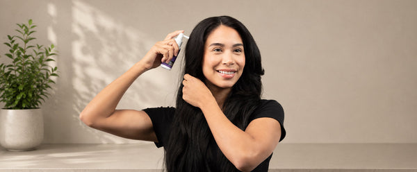 امرأة تفرق شعرها وتحمل أداة رش FOLIGAIN TRIOXIDIL بالقرب من فروة رأسها.