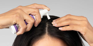 امرأة تفرق شعرها أثناء وضع علاج FOLIGAIN الموضعي على فروة رأسها